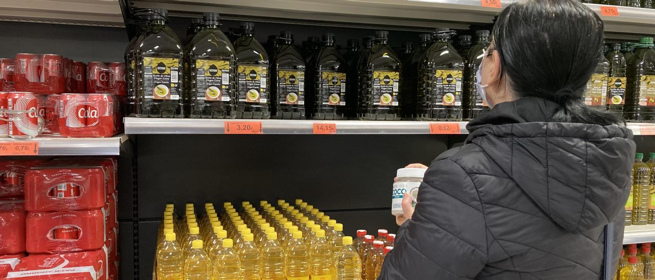 Una compradora revisa las estanterías del aceite en un supermercado.