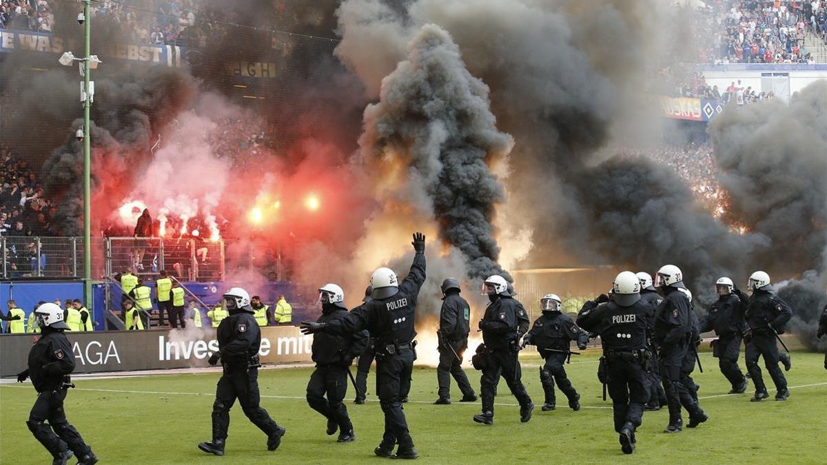 Antidisturbios saltan al césped del estadio del Hamburgo mientras en la grada se queman camisetas y banderas.