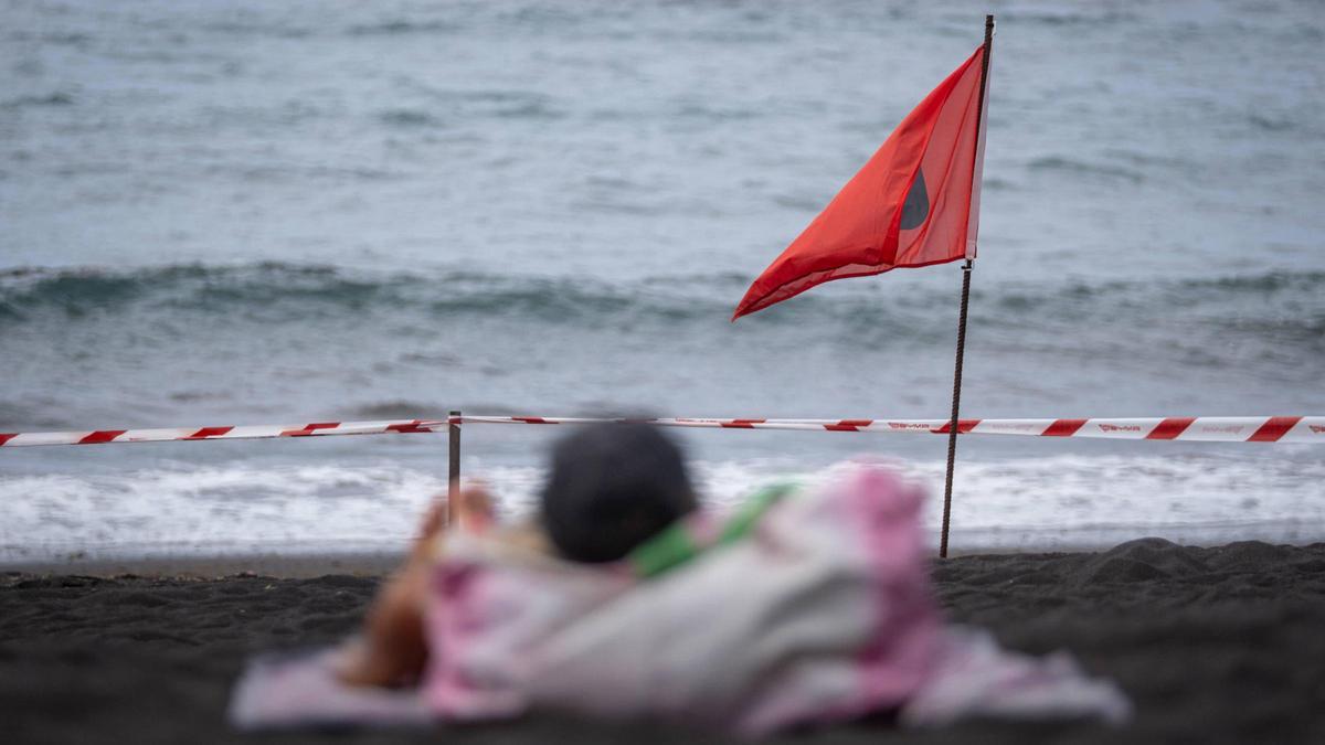 Una turista frente a la bandera roja que indica la prohibición de bañarse en Playa Jardín.