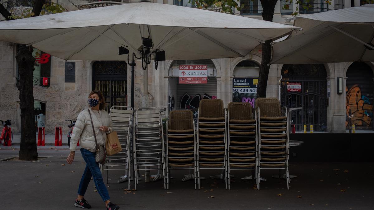 Archivo - Una mujer pasa junto a la terraza recogida de un bar cerrado