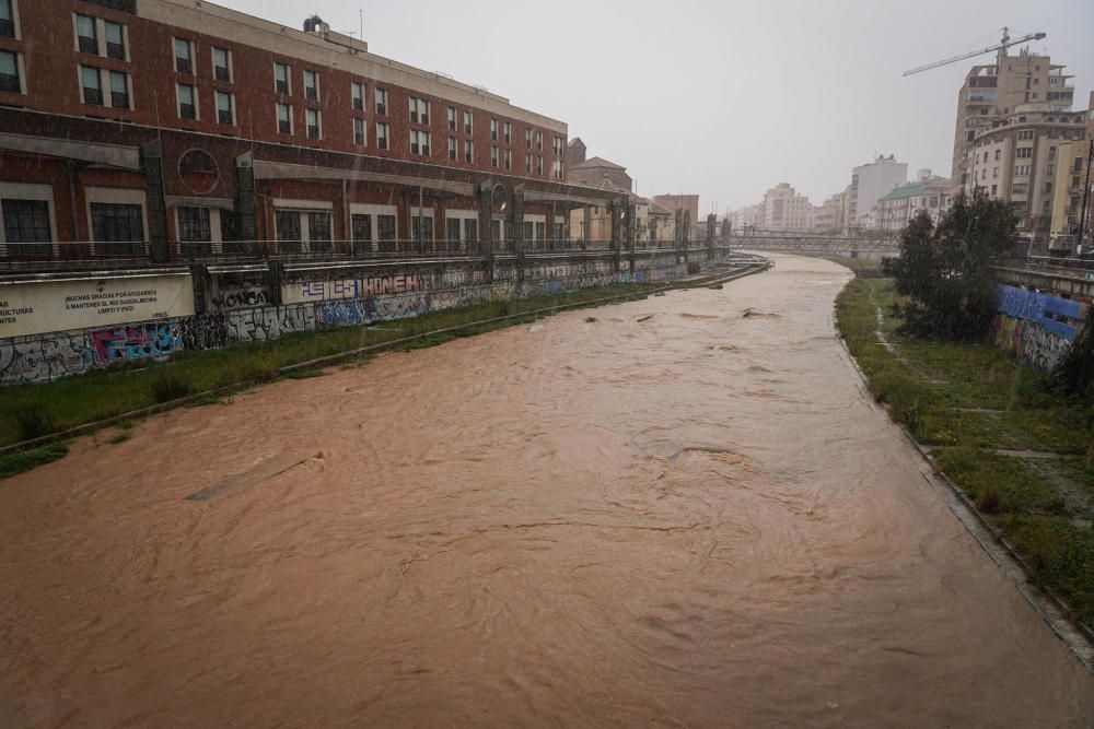 El río Guadalmedina crecido con agua y calles del Centro y el entorno del cauce, desiertas bajo la lluvia, la estampa de este martes 31 de marzo.