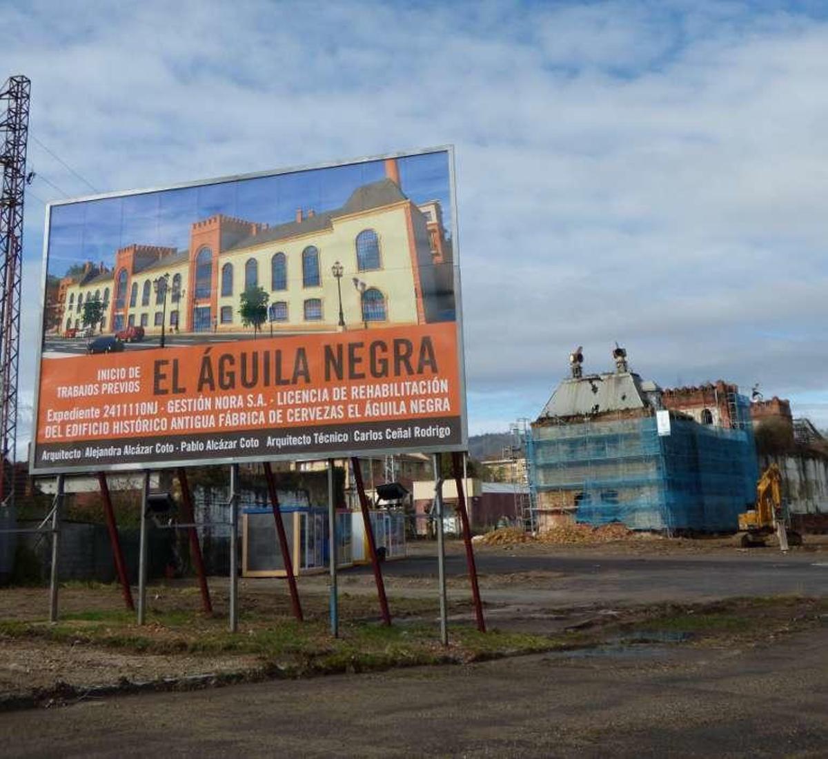 Cartel de información sobre las obras y, al fondo, máquinas y andamios.