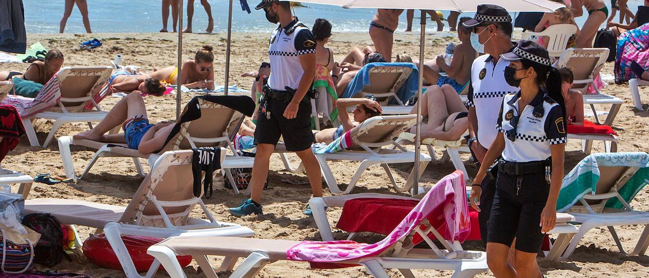 Tres agentes de la Policía Local vigilan este martes en la playa del Postiguet de Alicante para evitar robos y venta ilegal, y que se cumplan las medidas anticovid. | RAFA ARJONES