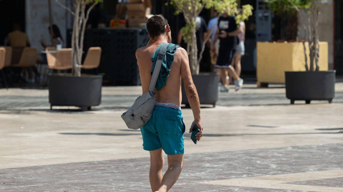 Un joven pasea sin camiseta por València debido al intenso calor.