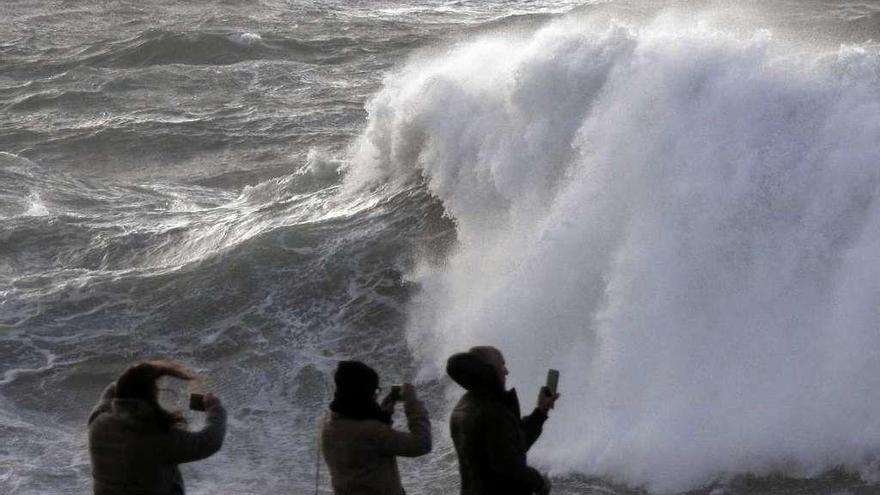 Varias personas graban las olas en la costa de Muxía.