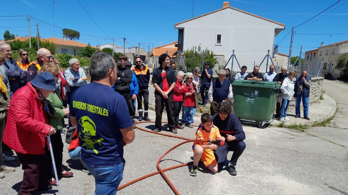 Un bombero muestra a un niño el funcionamiento de una manguera utilizada para apagar incendios ante la mirada de los vecinos-
