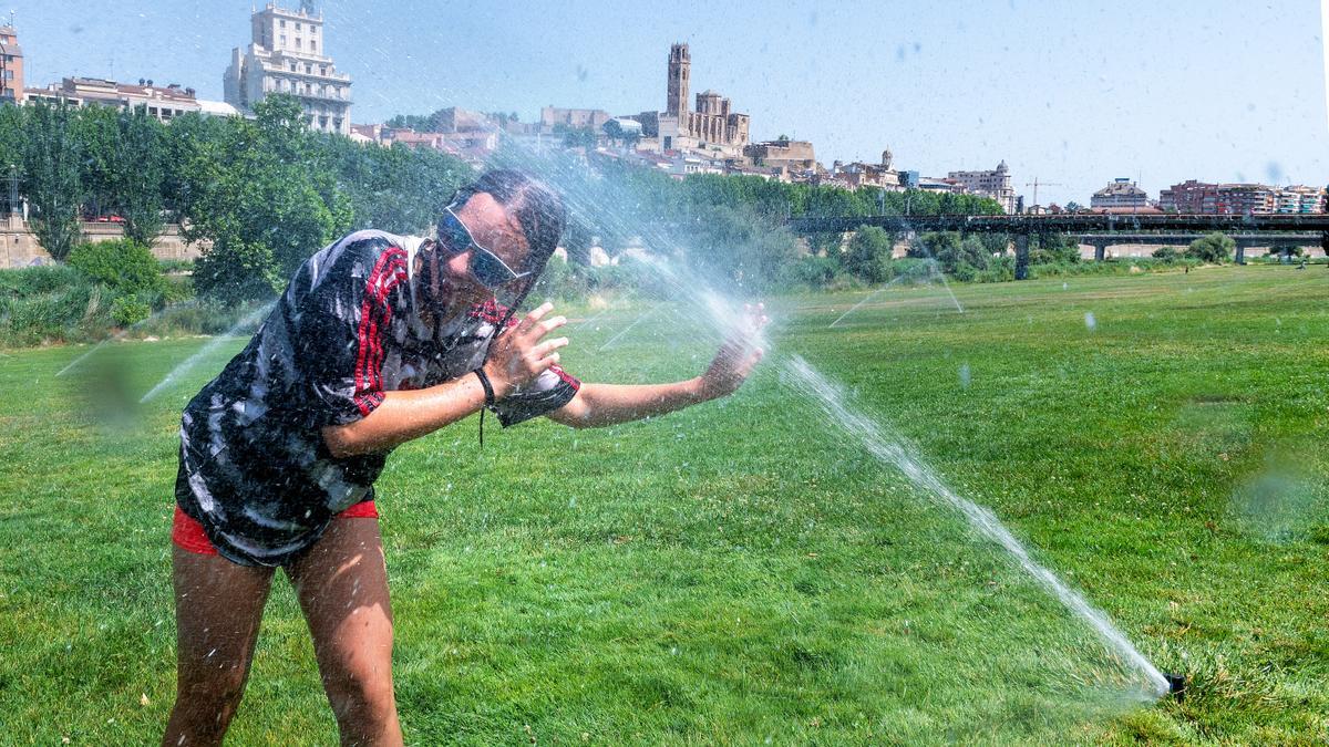 Una alumna del Col·legi del Carme, del barrio de la Bordeta de Lleida, aprovechan los aspersores de la canalización del Riu Segre, en el centro de Lleida, para refrescarse jugando