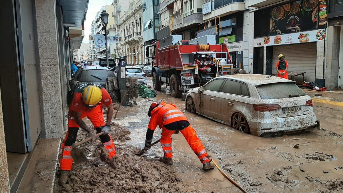 Dos bomberos forestales quitan lodo en una calle de Algemesí.