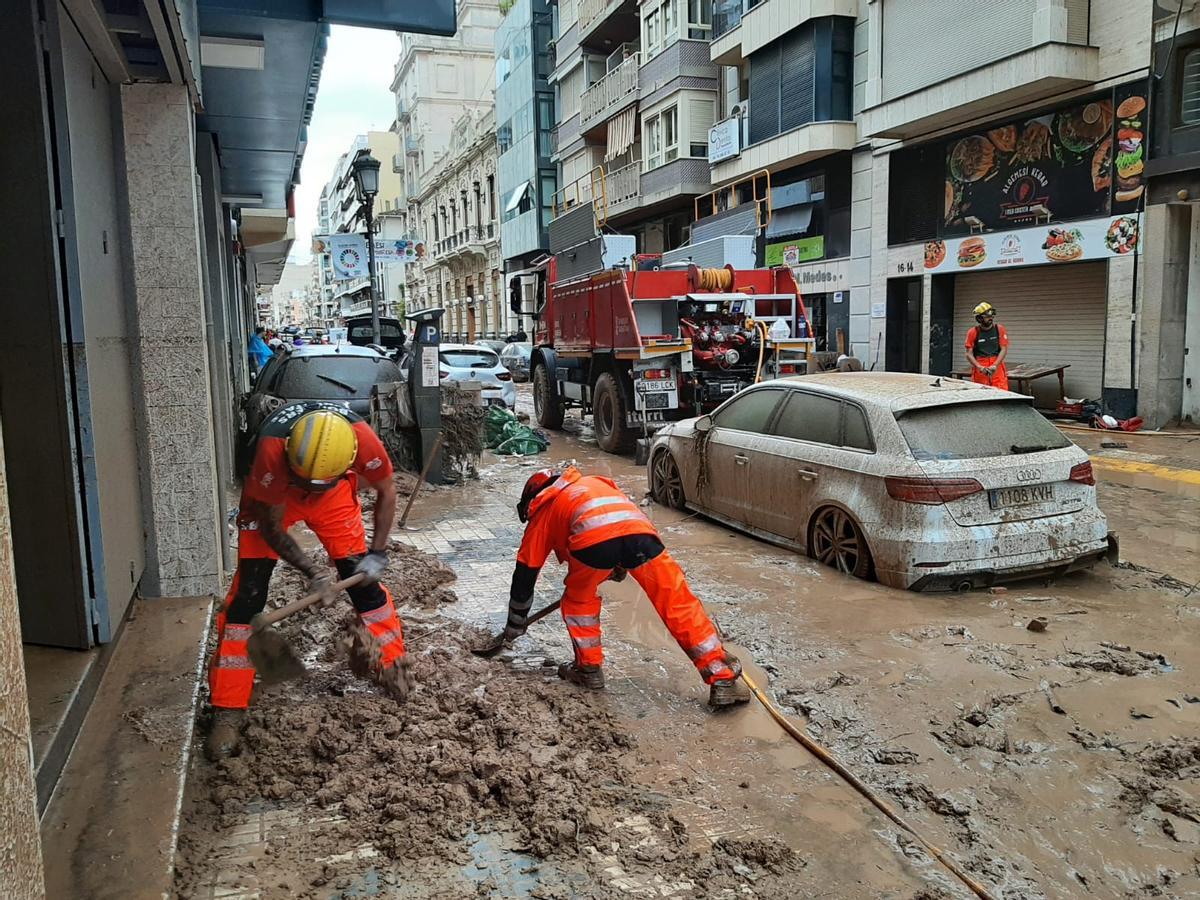 Dos bomberos forestales quitan lodo en una calle de Algemesí.