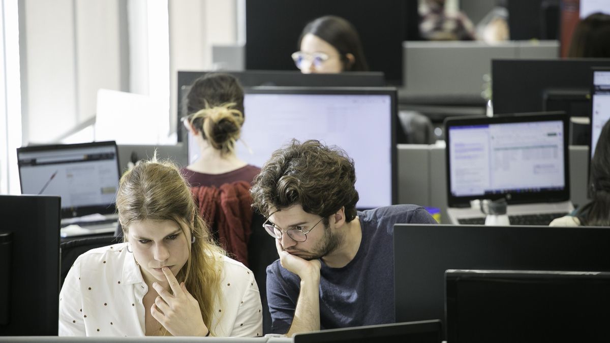 Una mujer y un hombre, en primer término, en sus puestos de trabajo en una empresa.