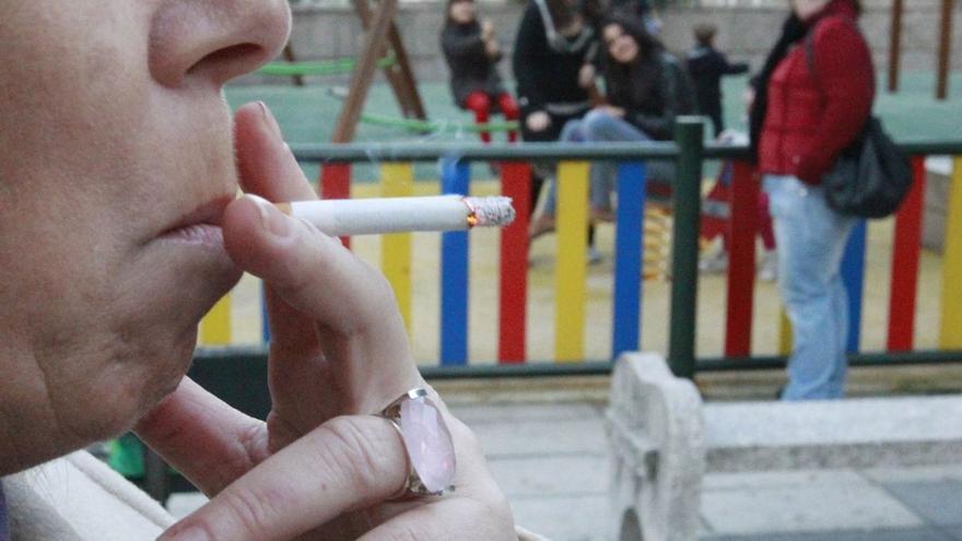 Una mujer da una calada a un cigarrillo, a cierta distancia de un parque infantil.  | // RICARDO GROBAS