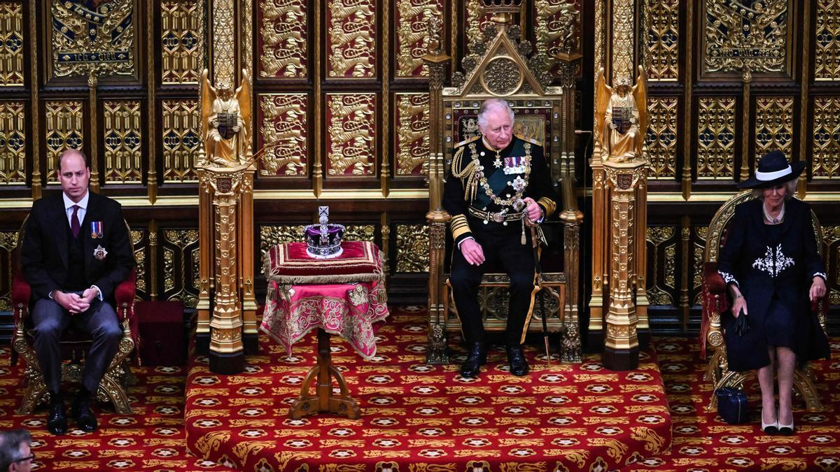 El Príncipe Carlos, Príncipe de Gales de Gran Bretaña (2.º a la derecha) se sienta junto a la Corona del Estado Imperial (2.º a la izquierda) con el Príncipe Guillermo, Duque de Cambridge (a la izquierda) de Gran Bretaña y Camilla, Duquesa de Cornualles (a la derecha) de Gran Bretaña en la Cámara de los Lores, durante la Apertura Estatal del Parlamento, en las Casas del Parlamento, en Londres, el 10 de mayo de 2022