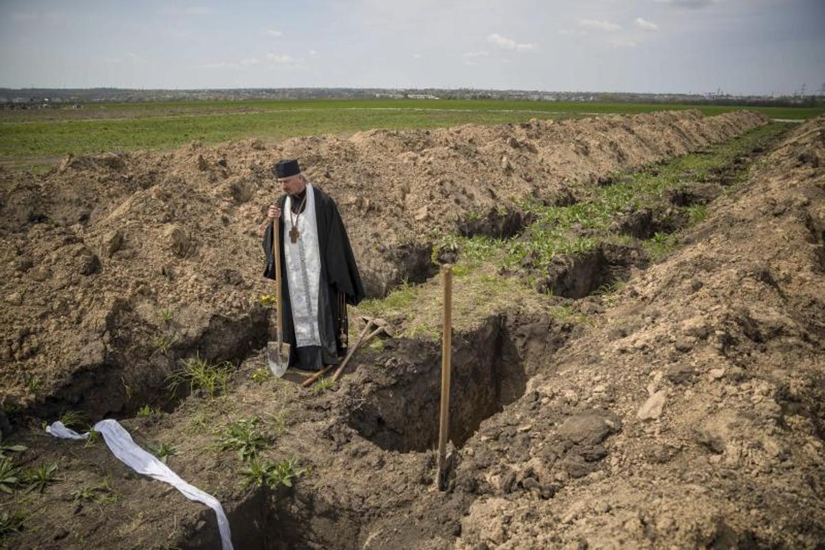 Un religioso ortodoxo, pala en mano, observa fosas nuevas para caídos en combate en el cementerio militar de Dnipro (Ucrania) en mayo de 2022.