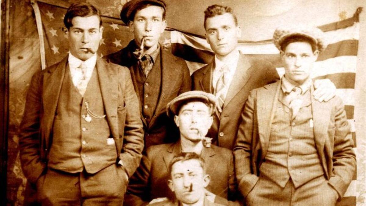 Uns joves de Tàrbena fotografiats cap al 1920, ben elegants, fumant puros i lluint rellotges de cadena. Darrere, la bandera americana. Volien retratar el seu èxit.
