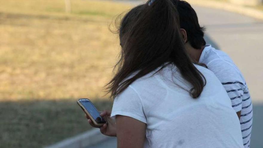 Dos adolescentes consultan un teléfono móvil.