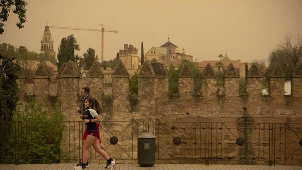 Dos personas hacen deporte bajo un cielo con calima en las murallas de Córdoba.