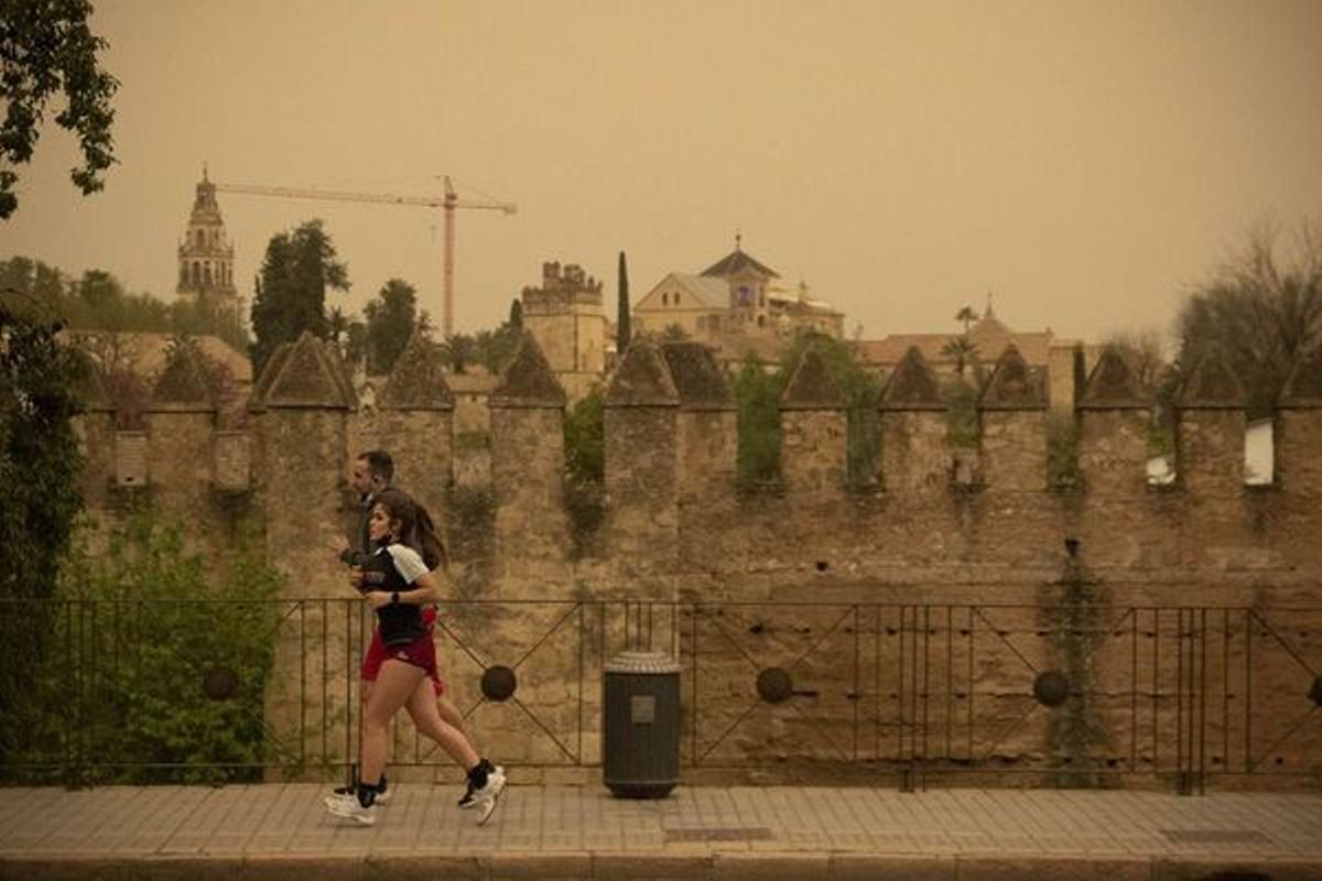 Dos personas hacen deporte bajo un cielo con calima en las murallas de Córdoba.
