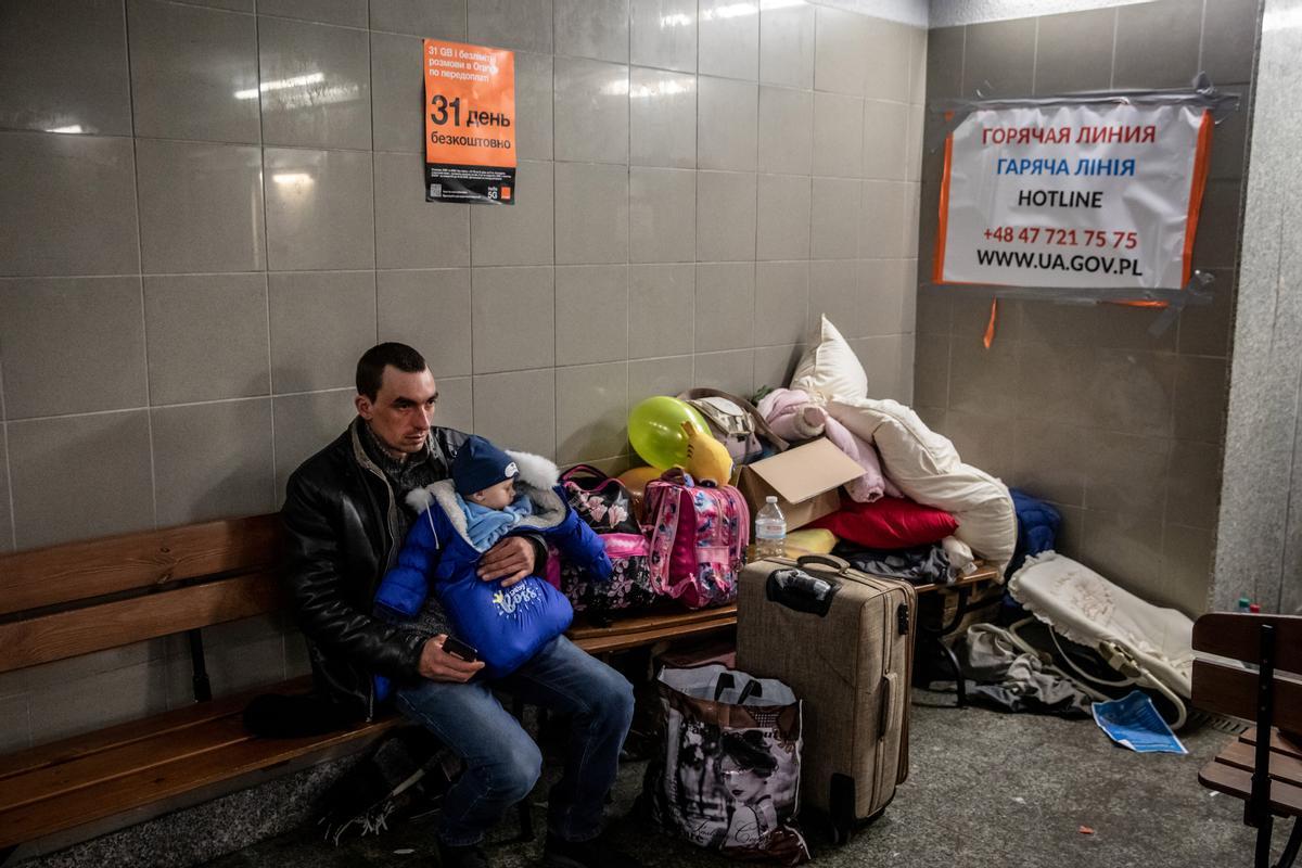 Un hombre procedente de Ucrania sostiene a su hijo, en el interior de la estación de tren de Przemysl, Polonia.