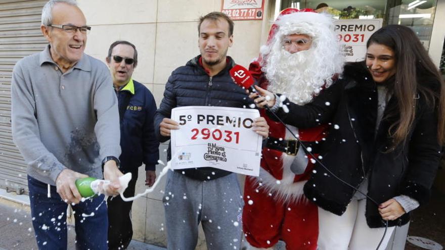 El joven agraciado, con el cartel del número premiado mientras el estanquero descorcha una botella