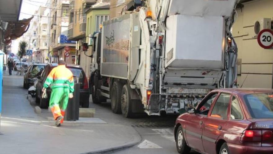 Un turismo espera que el camión de la basura cargue en una calle de Torrevieja.