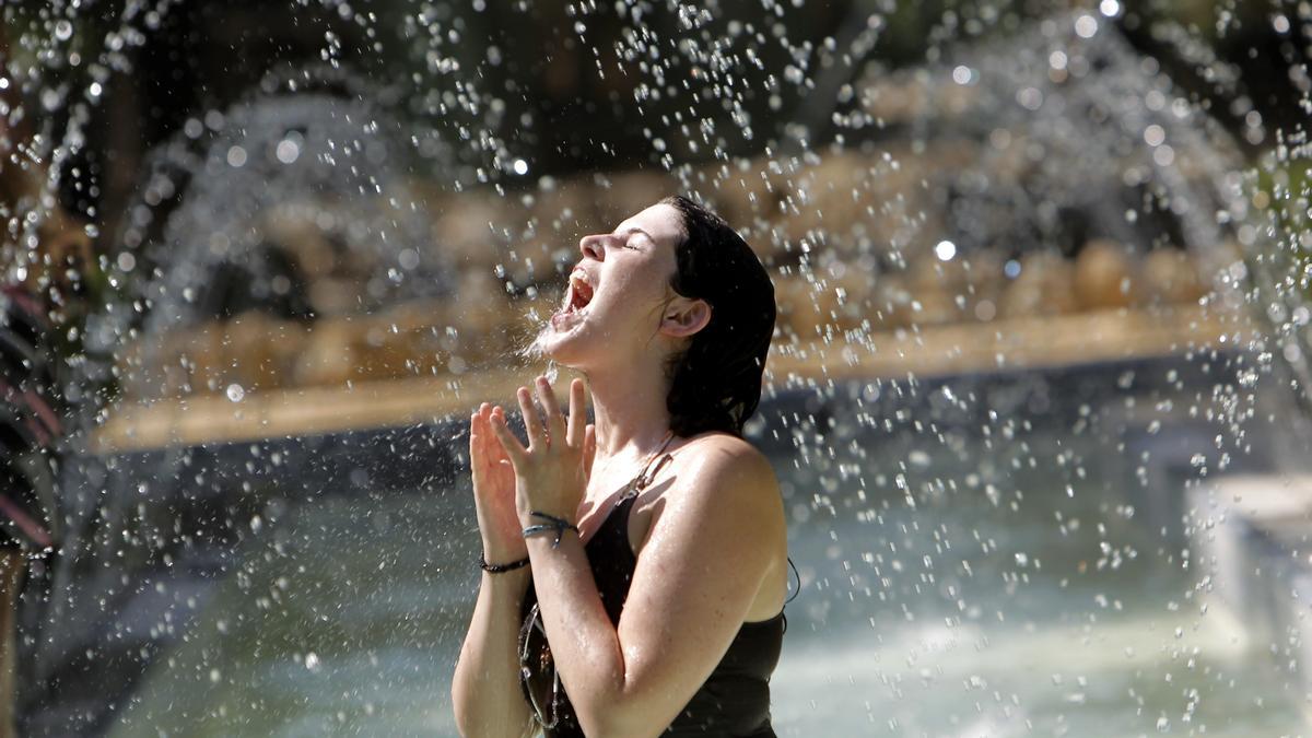 Una joven se refresca en una fuente durante una ola de calor.