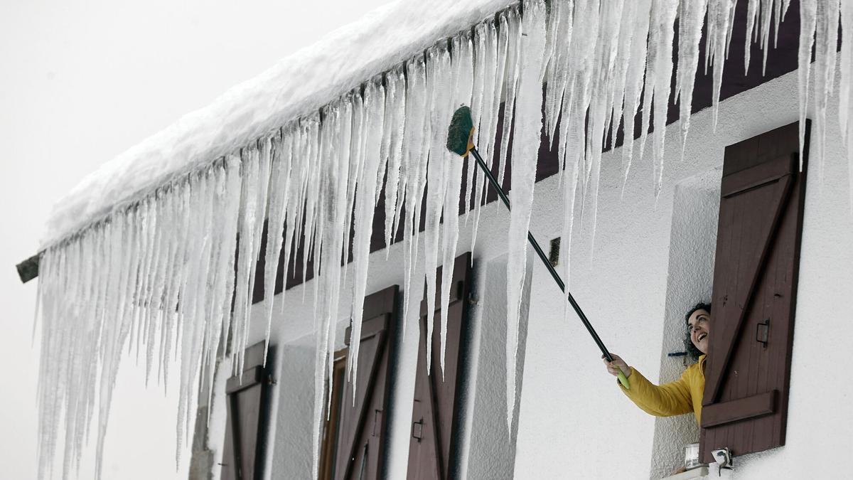 Una persona abre la ventana de su casa, donde grandes carámbanos de hielo penden del tejado, en una imagen de archivo.