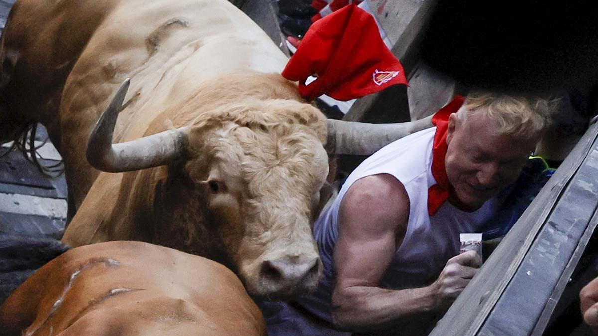 Un mozo es alcanzado por uno de los toros de la ganadería gaditana Núñez del Cuvillo a su llegada a la curva de la calle Estafeta durante el primer encierro de los Sanfermines 2022.