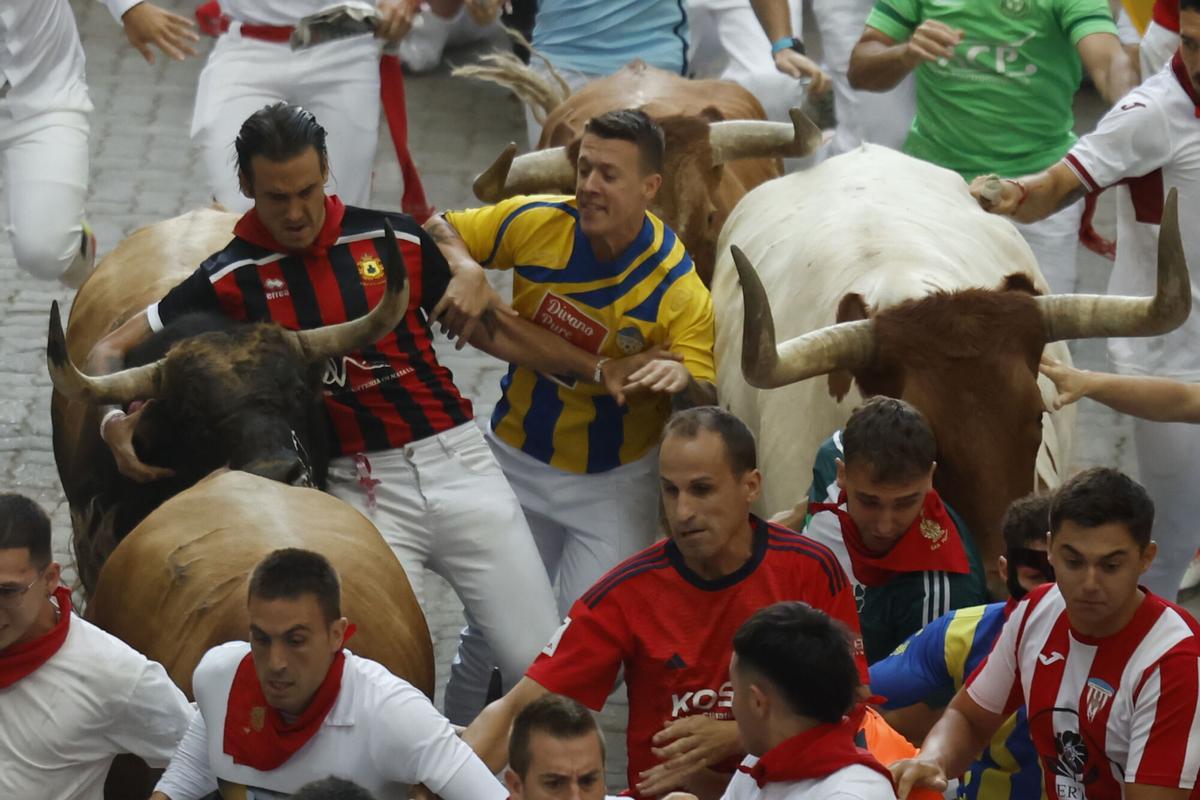 Dos mozos corren junto a los toros de la ganadería gaditana de La Palmosilla antes de entrar en el Callejón durante el sexto encierro de los Sanfermines 2026, este domingo en Pamplona. EFE/Jesús Diges