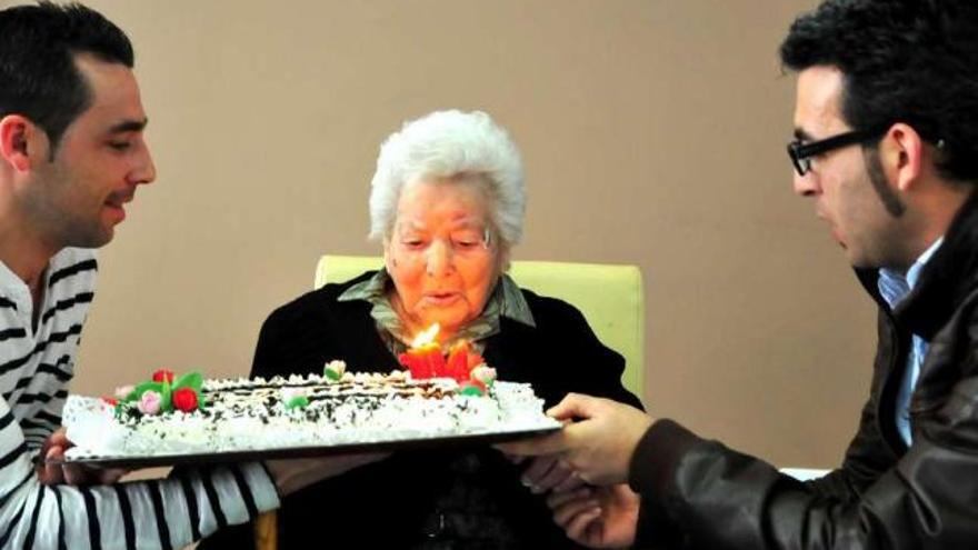 Eugenia Martínez, de 104 años, sopla las velas de la tarta que le acercan sus nietos.  // I.Abella