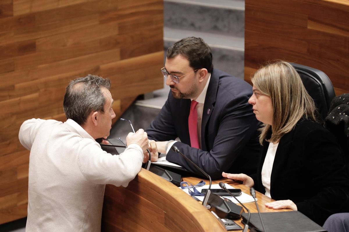 El presidente asturiano y secretario general de la FSA, Adrián Barbón, conversa con el consejero de Ordenación del Territorio y coordinador de IU, Ovidio Zapico, en un receso en la Junta General. A la derecha, Gimena Llamedo González, vicepresidenta del Gobierno