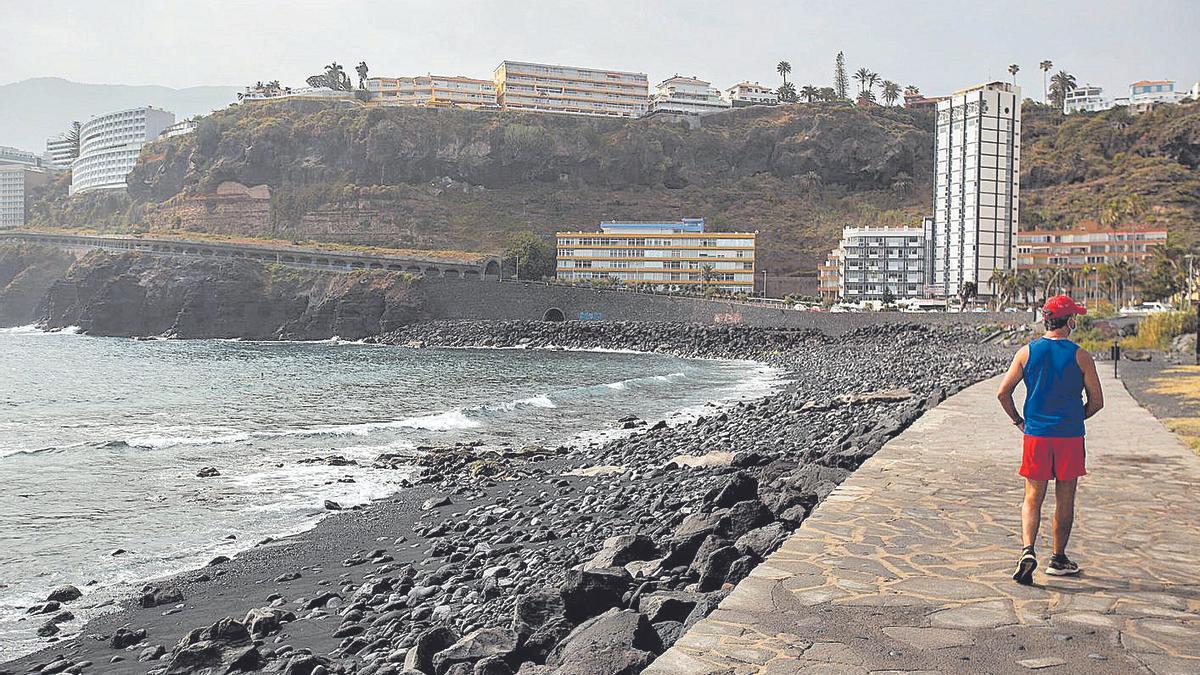 Un hombre pasea por la playa de Martiánez, al fondo se ve la ladera del mismo nombre.