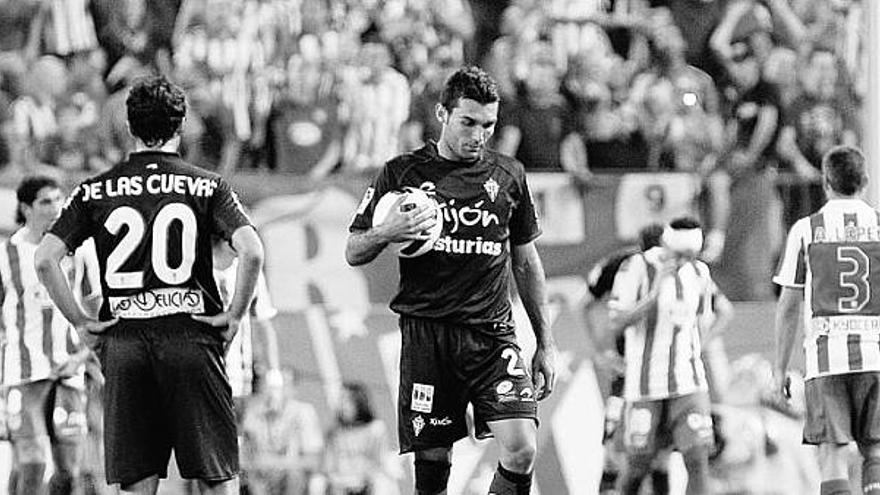 Barral lleva el balón en la mano para sacar de centro, con De las Cuevas de espaldas, tras un gol del Atlético.