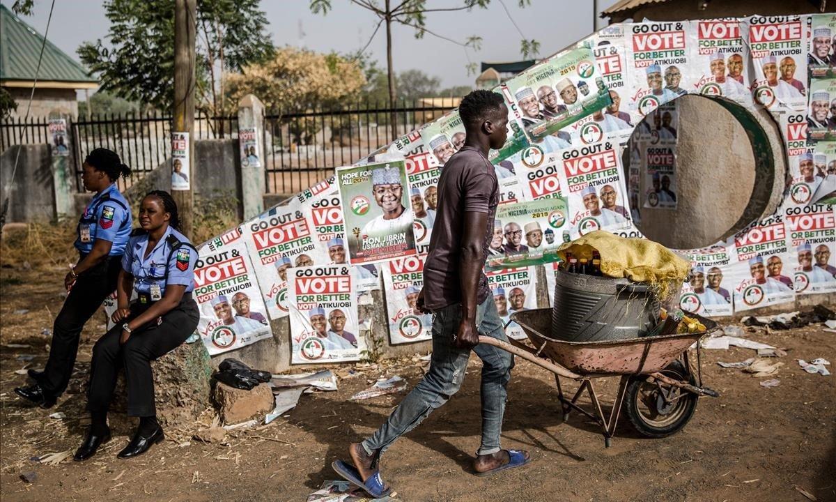 Un hombre pasa delante de mujeres policía al llegar para vender bebidas durante el mitin del Partido Democrático Popular de la oposición en la plaza Ribadu en el estado de Jimeta Adamawa, Nigeria.