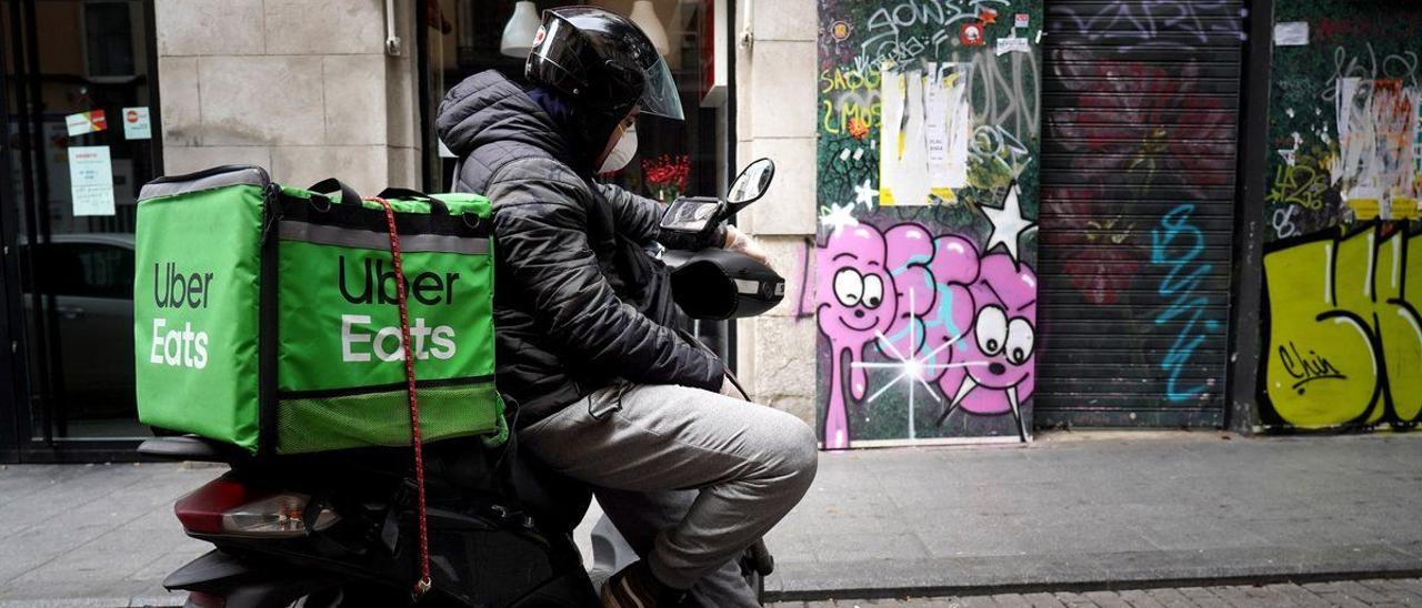 Un repartidor de UberEats espera un pedido en su motocicleta.