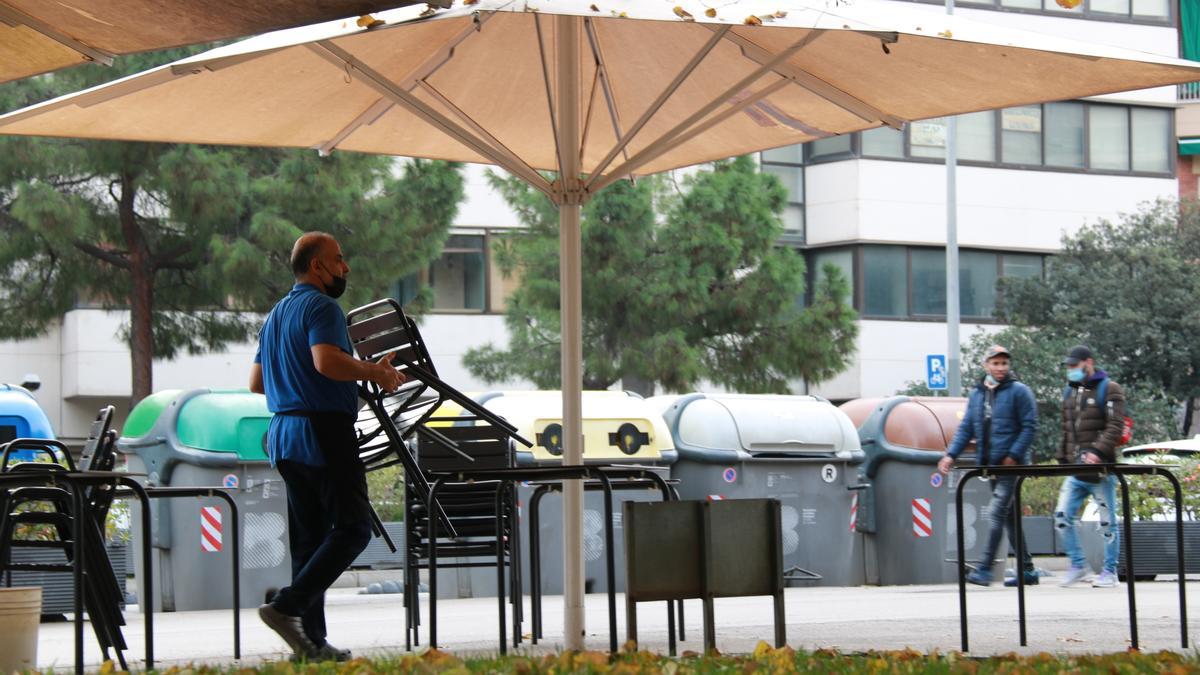 Pla obert d&#039;un cambrer col·locant taules i cadires a la terrassa d&#039;un restaurant del passeig Sant Antoni de Barcelona, al barri de Sants