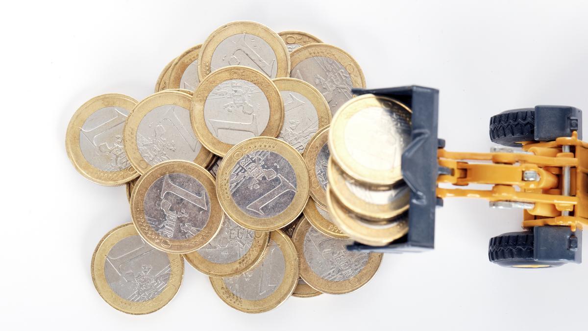 Varias monedas de un euro junto a una excavadora pequeña