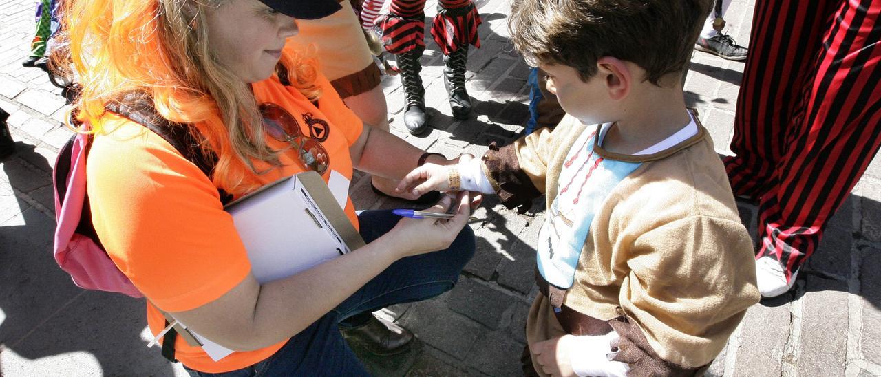 Una componente de Protección Civil coloca a un pequeño una pulsera identificativa para el Carnaval.