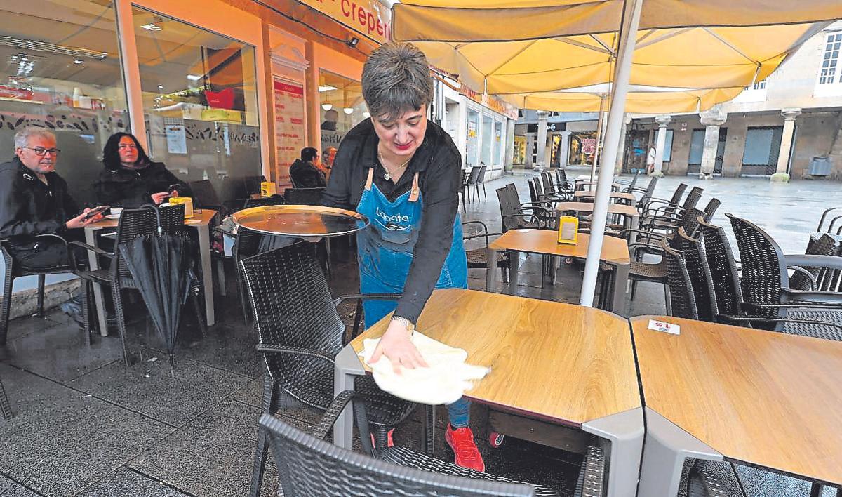 Una de las camareras de La Nata limpia una mesa en una terraza medio vacía.