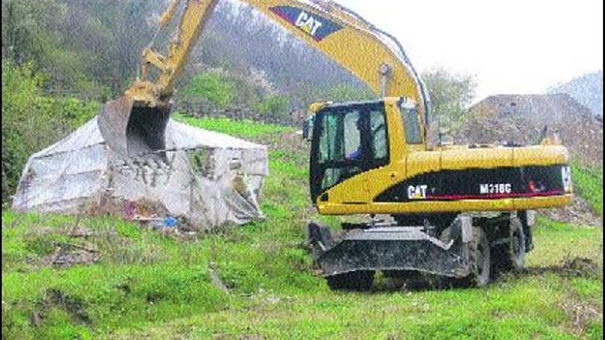 Una máquina derriba una viaja chabola, con la caja de la carretera al fondo.