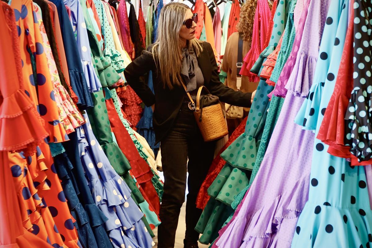 SEVILLA, 10/04/2024.- Una mujer entre trajes de flamenca hoy en una tienda en Sevilla. Trajes de flamenca con lentejuelas y más manga corta que en años anteriores llegan a la Feria de Abril de Sevilla este 2024 a abrirse paso entre volantes y los tradicionales lunares. EFE/ José Manuel Vidal