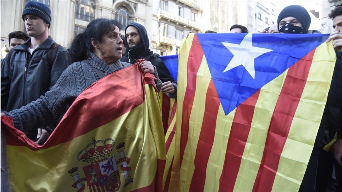 Una señora muestra la bandera española ante una joven con el rostro tapado que exhibe una estelada.
