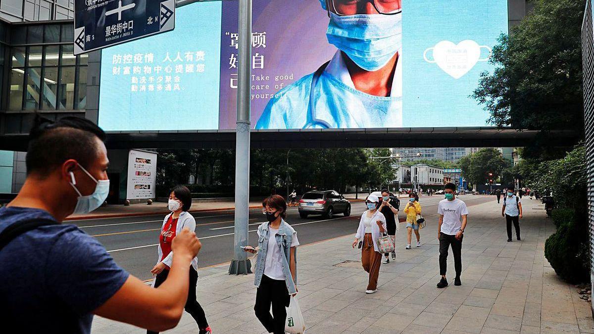 Varias personas caminan bajo un anuncio de un centro comercial de Pekín.