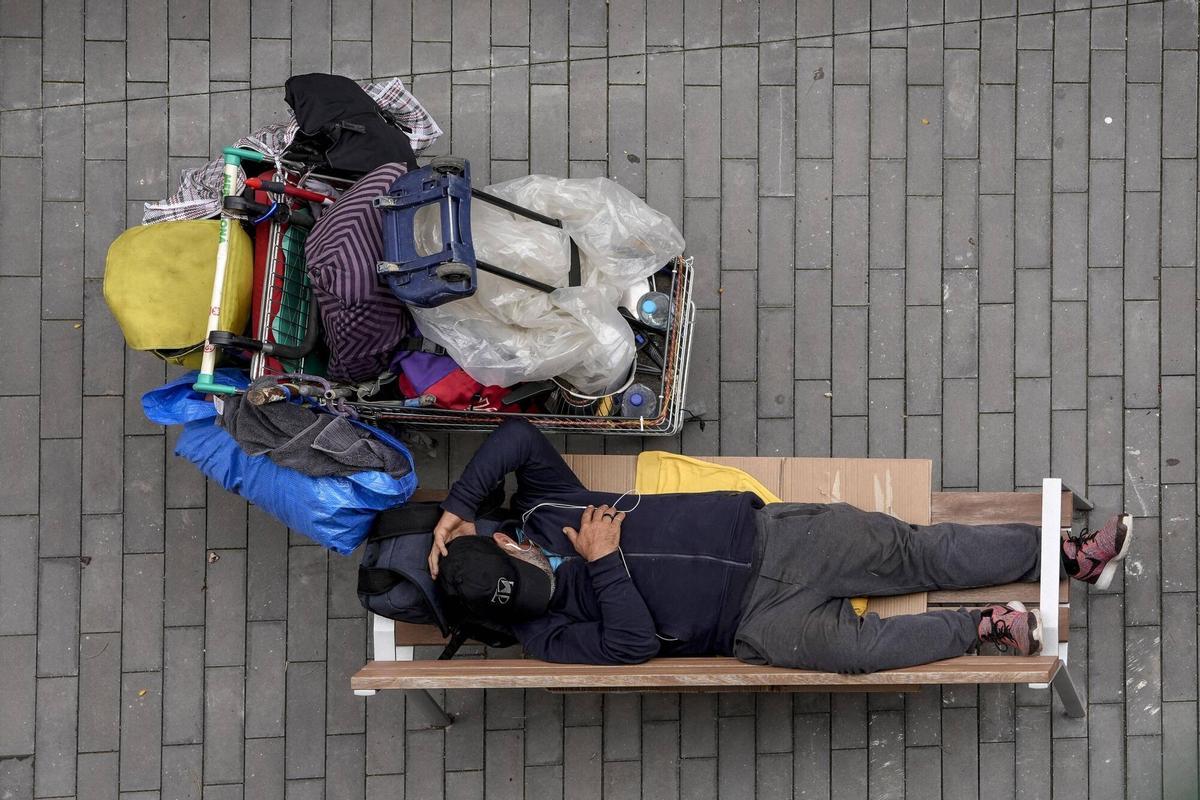 Una persona sense llar dorm en un banc d’una plaça del Poblenou