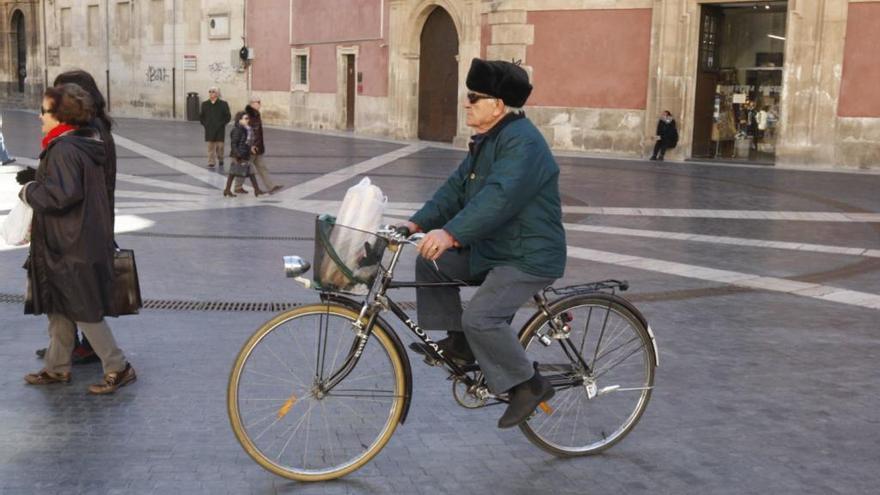 Un hombre abrigado circula en bicicleta por la Plaza de Belluga. / Juan Caballero