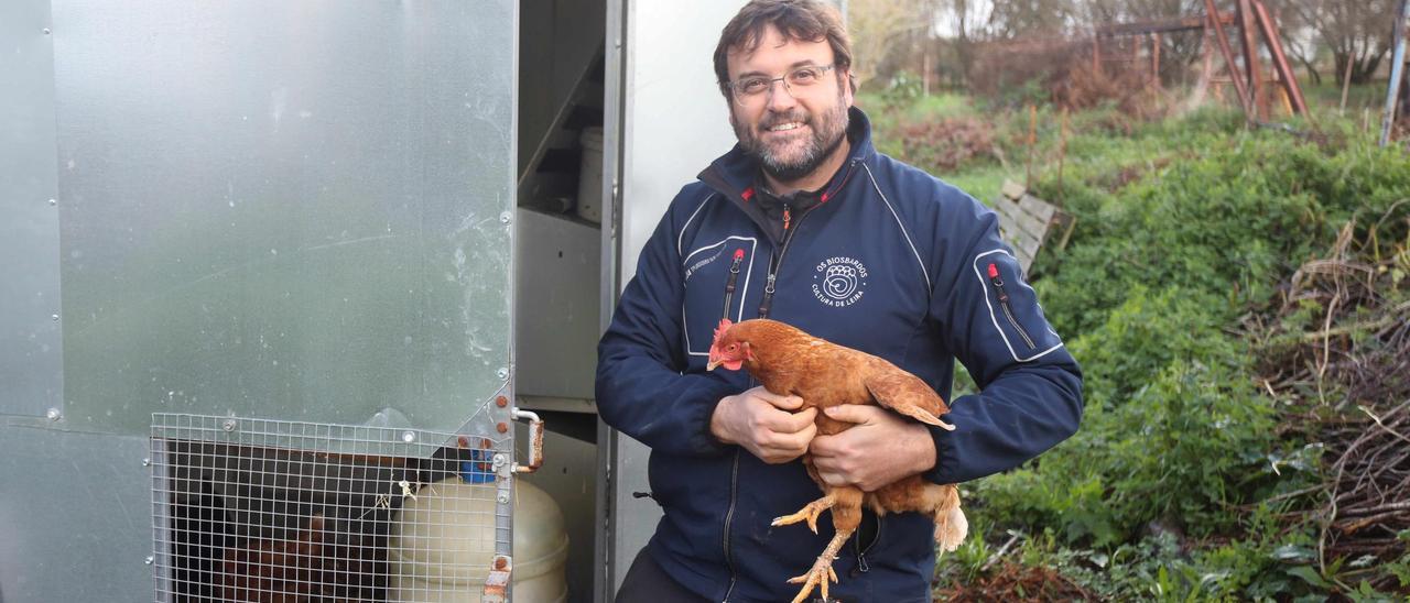 El fundador de Os Biosbardos, Miguel Ángel Roig, con una de sus gallinas, junto al &quot;gallinero inteligente&quot; que desarrolla.