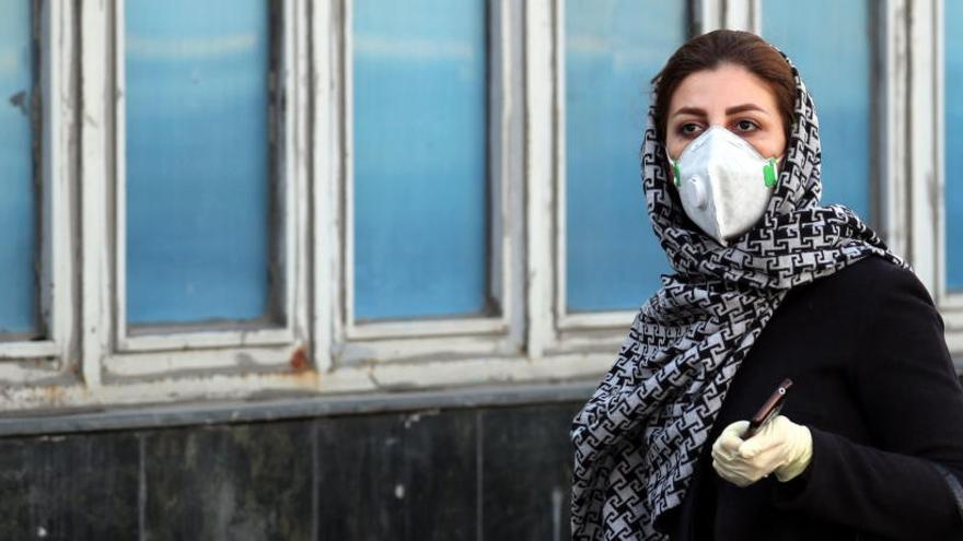 Una mujer iraní con mascarilla y guantes protectores camina en Teherán.