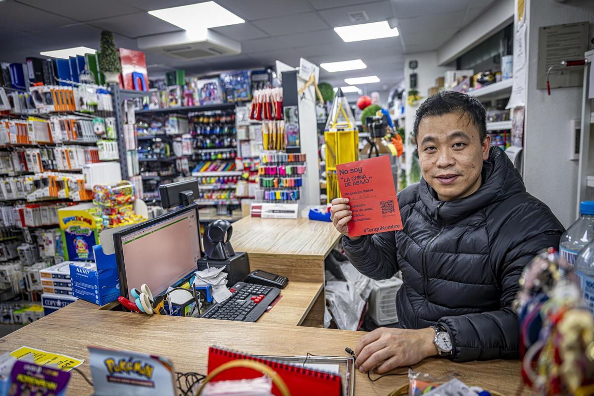 El propietario de un bazar de Barcelona muestra uno de los carteles de la iniciativa #TengoNombre