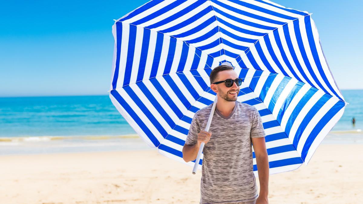 Un joven con gafas de sol camina por la playa con una sombrilla.