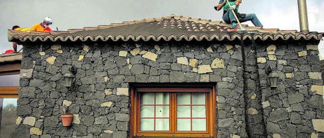 Un operario retira la ceniza acumulada en el techo de una vivienda próxima al volcán.