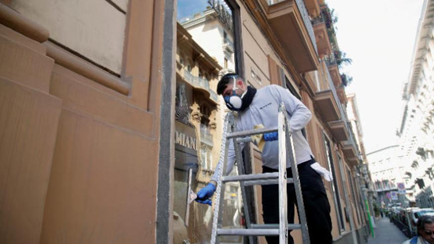 Un hombre limpia un escaparate protegido por una mascarilla en Nápoles.